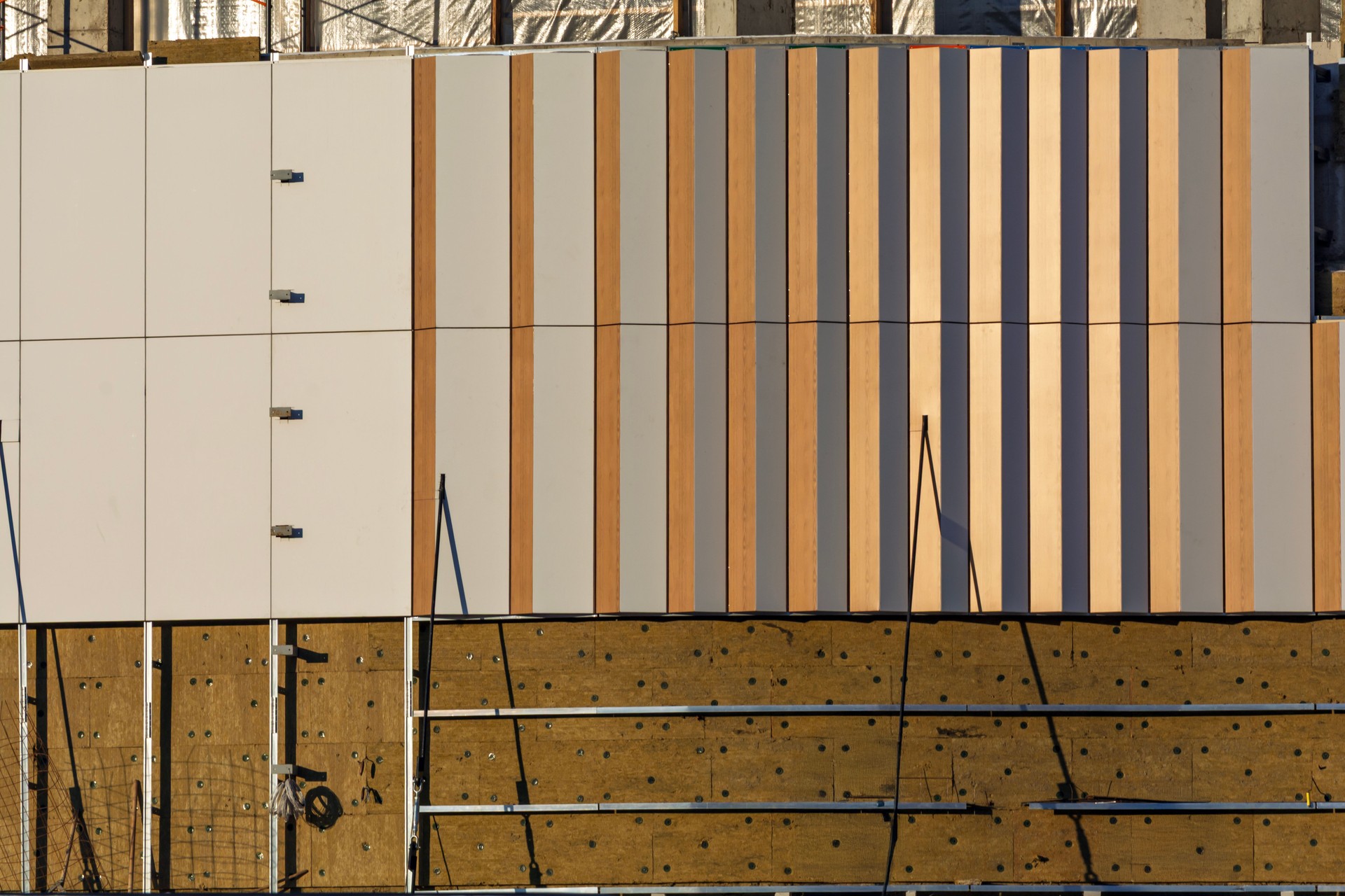 A building facade under cladding installation with decorative panels and vertical stripes. Sun reflection highlights the texture.